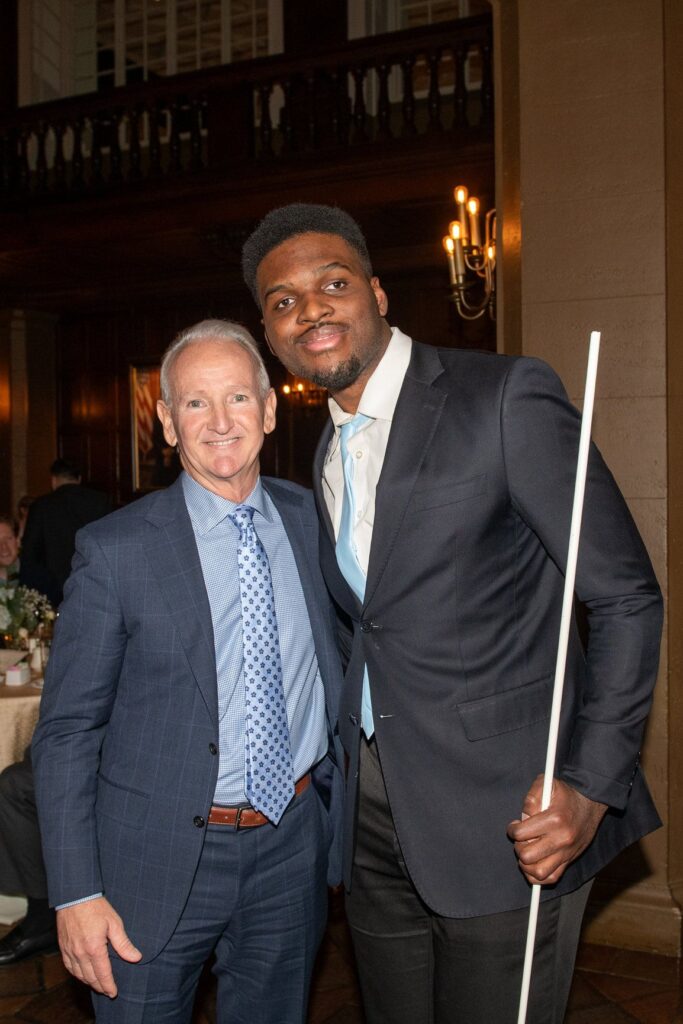 A photo of Tim Olukanni (right) with Albion CEO, Brian Newsome (left) at TAD Gala in 2024. Both are dressed nicely in three piece suits and blue ties. 